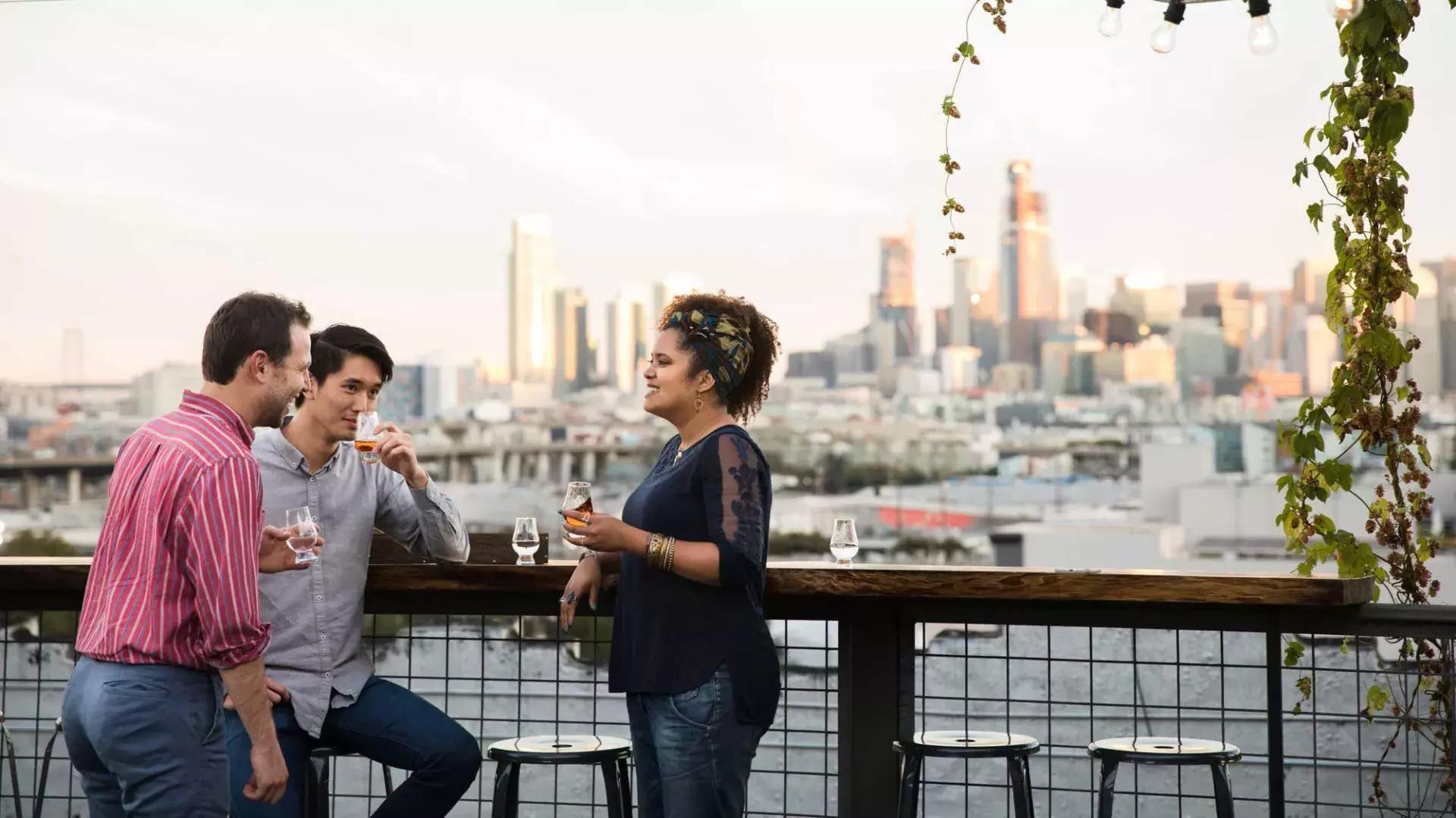 在贝博体彩app的Anchor Distilling屋顶上，三个人围坐在一张户外桌子旁, 加州.