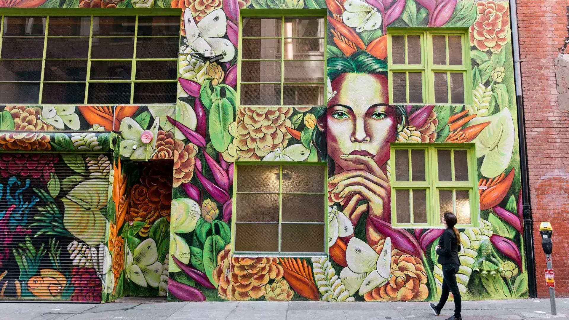 A woman looks up at a brightly colored mural on the side of a brick building in San Francisco.