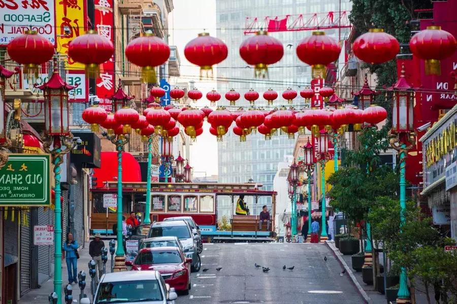 A hilly street in San Francisco's Chinatown is pictured with red lanterns dangling and a streetcar passing by.